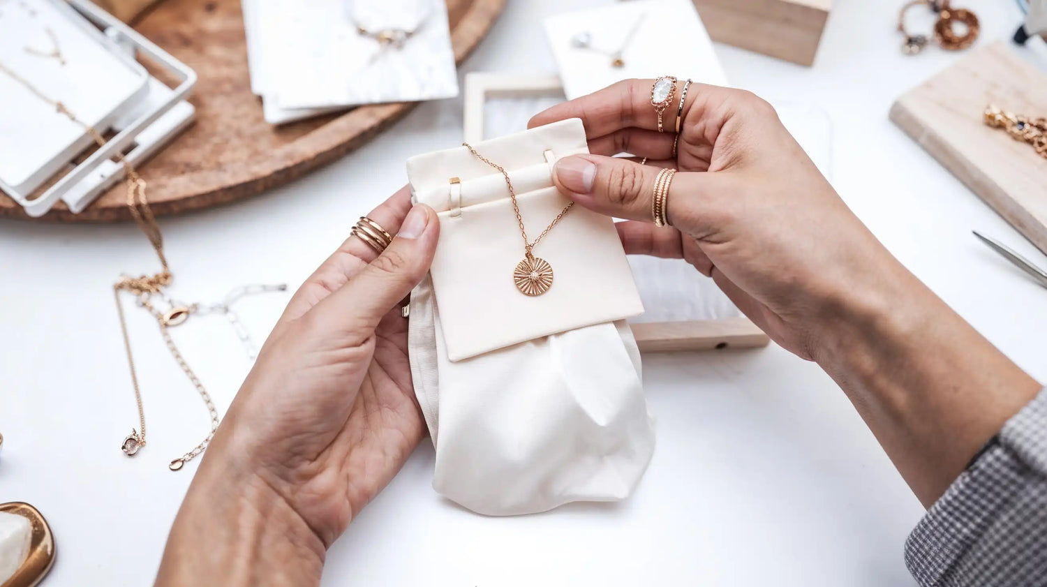 Nahaufnahme von Händen, die eine Mercy’s Jewelry Halskette mit goldenem Anhänger in einem Schmuckpouch präsentieren