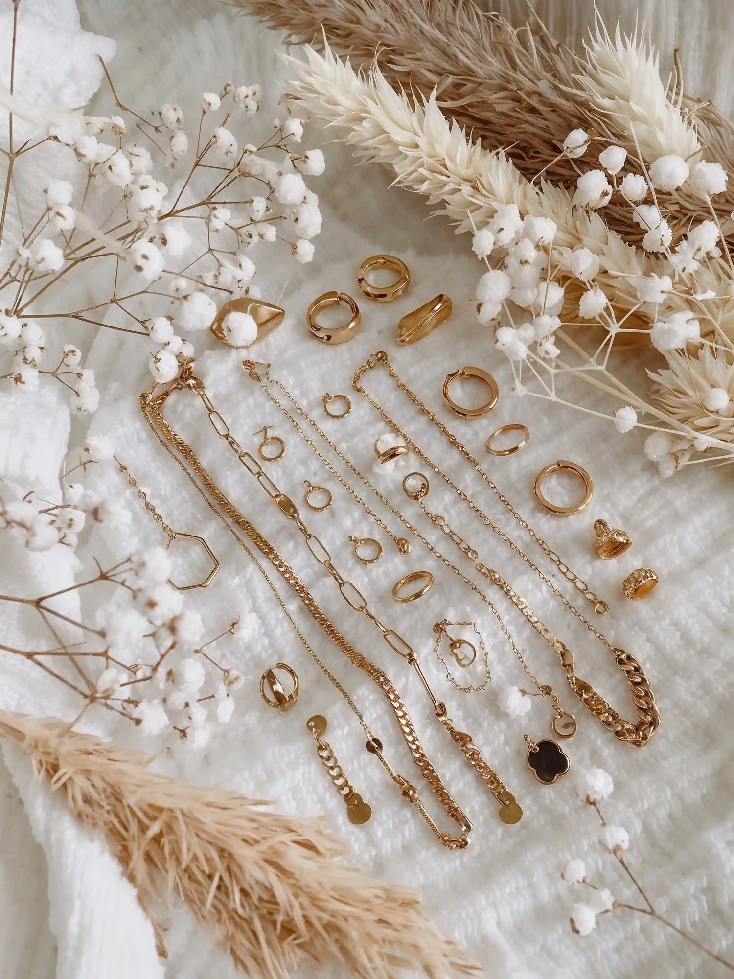Goldschmuck wie Ketten, Ringe und Armbänder dekorativ auf weißem Untergrund mit Trockenblumen – Schmuckpflegeguide von Mercy’s Jewelry