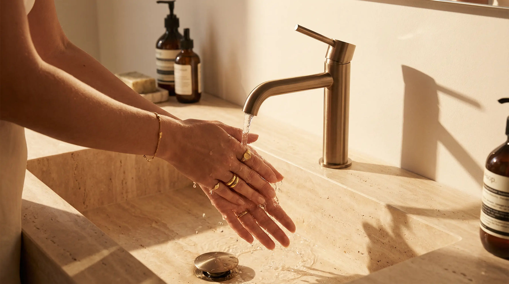 Goldene Ringe und zartes Armband aus vergoldetem Edelstahl am Handgelenk beim Händewaschen unter fließendem Wasser