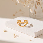 Chevron-Ring aus Edelstahl 18 K vergoldet, offen und verstellbar, mit gedrehter Struktur auf heller Steinplattform und Trockenblumen im Hintergrund – Soriel Ring | Mercy’s Jewelry