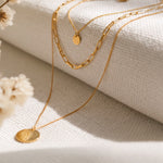 Dreireihige Gliederkette mit rundem Anhänger aus Edelstahl 18 K vergoldet, liegt auf hellem Stoff mit sanftem Licht und Trockenblumen – Sienna Layers Kette | Mercy’s Jewelry