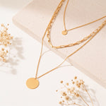 Dreireihige Gliederkette mit rundem Anhänger aus Edelstahl 18 K vergoldet, liegt auf heller Steinplatte mit Trockenblumen im Sonnenlicht – Sienna Layers Kette | Mercy’s Jewelry