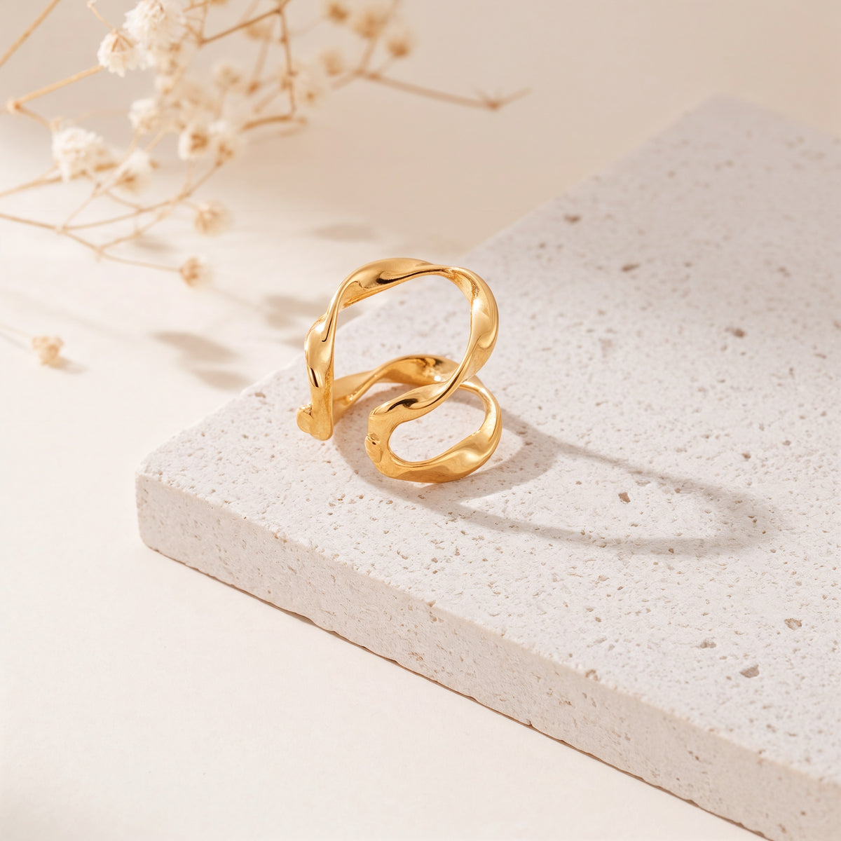 Earcuff mit geschwungener Form aus Edelstahl 18 K vergoldet, liegt auf heller Steinplatte mit Trockenblumen im warmen Tageslicht – Nirel Earcuff | Mercy’s Jewelry