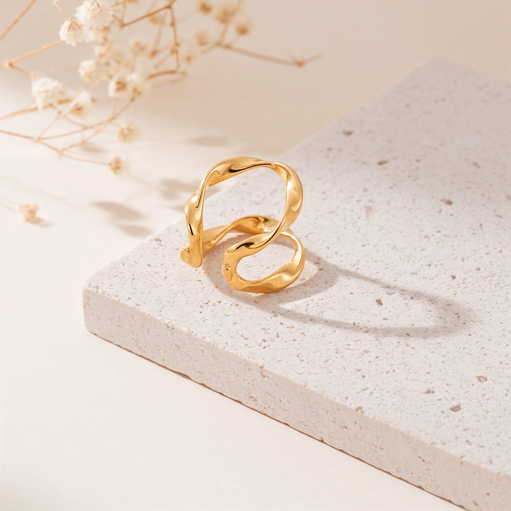 Earcuff mit geschwungener Form aus Edelstahl 18 K vergoldet, liegt auf heller Steinplatte mit Trockenblumen im warmen Tageslicht – Nirel Earcuff | Mercy’s Jewelry