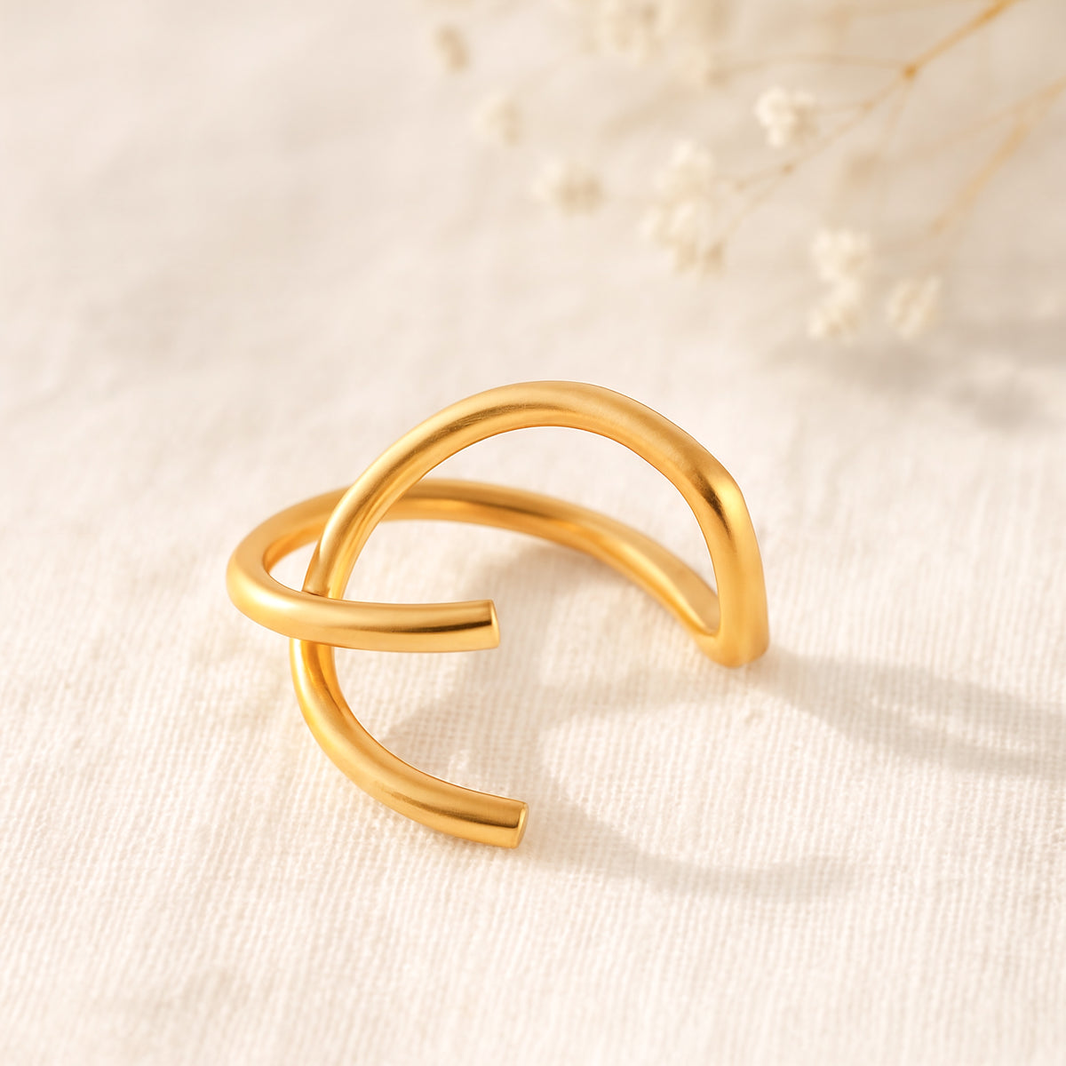 Minimalistischer Earcuff mit offenem Design aus Edelstahl 18 K vergoldet, liegt auf hellem Stoff mit sanftem Licht und Trockenblumen im Hintergrund – Nuvin Earcuff | Mercy’s Jewelry