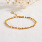 Feines gedrehtes Armband aus Edelstahl 18 K vergoldet mit glänzender Oberfläche, elegant auf hellem Stoff mit Trockenblumen – Solira Armband | Mercy’s Jewelry