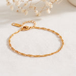 Feines Rope-Armband aus Edelstahl 18 K vergoldet mit gedrehter Struktur, liegend auf hellem Stoff mit Trockenblumen – Fayara Armband | Mercy’s Jewelry