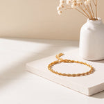 Feines, gedrehtes Armband aus Edelstahl 18 K vergoldet, auf heller Steinplatte mit Vase und Trockenblumen im Sonnenlicht – Solira Armband | Mercy’s Jewelry