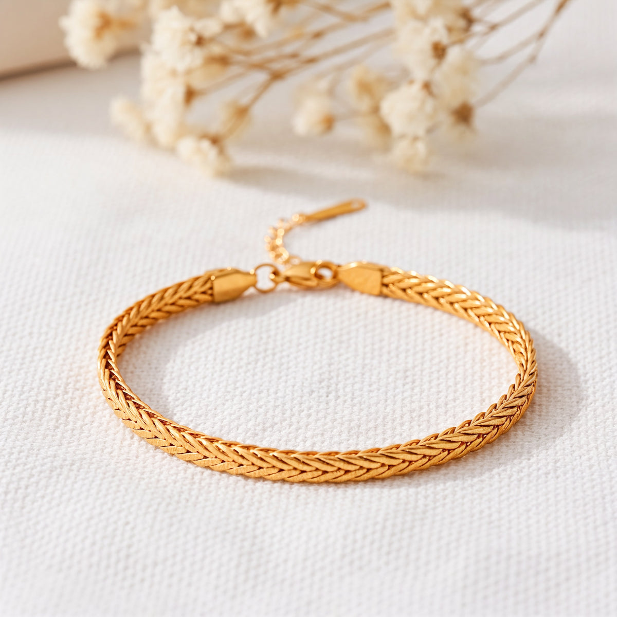 Geflochtenes Armband aus Edelstahl 18 K vergoldet mit dichter Kettenstruktur, elegant auf hellem Stoff mit Trockenblumen – Kaelwyn Armband | Mercy’s Jewelry