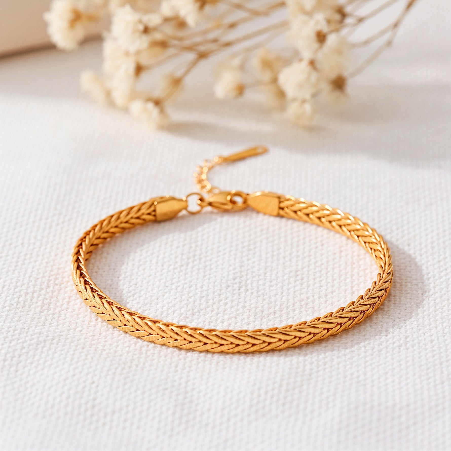 Geflochtenes Armband aus Edelstahl 18 K vergoldet mit dichter Kettenstruktur, elegant auf hellem Stoff mit Trockenblumen – Kaelwyn Armband | Mercy’s Jewelry