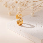 Gekreuzter Ring aus Edelstahl 18 K vergoldet, offen und verstellbar, mit elegant geschwungenem Design auf heller Steinplattform mit Trockenblumen im Hintergrund – Elanira Ring | Mercy’s Jewelry