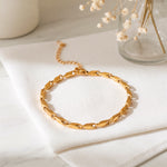 Gliederarmband aus Edelstahl 18 K vergoldet mit flachen, geschwungenen Gliedern, liegend auf weißem Stoff mit Glasvase und Trockenblumen im Hintergrund – Talea Armband | Mercy’s Jewelry