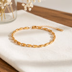 Gliederarmband aus Edelstahl 18 K vergoldet mit flachen, eleganten Gliedern, liegend auf hellem Stoff mit Trockenblumen im Hintergrund – Talea Armband | Mercy’s Jewelry