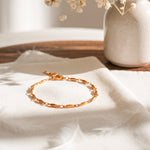 Feines Gliederarmband aus Edelstahl 18 K vergoldet mit ovalen, glänzenden Gliedern, liegend auf weißem Stoff neben Vase und Trockenblumen im Sonnenlicht – Mireya Armband | Mercy’s Jewelry