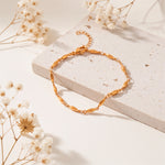 Feines Gliederarmband aus Edelstahl 18 K vergoldet mit ovalen, glänzenden Gliedern, liegend auf hellem Steinuntergrund mit weißen Trockenblumen im Hintergrund – Mireya Armband | Mercy’s Jewelry