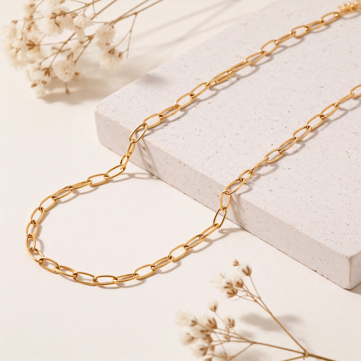 Goldene Gliederkette aus Edelstahl 18K vergoldet, liegt auf heller Steinplatte mit getrockneten Blumen im Hintergrund – Marva Necklace | Mercy’s Jewelry