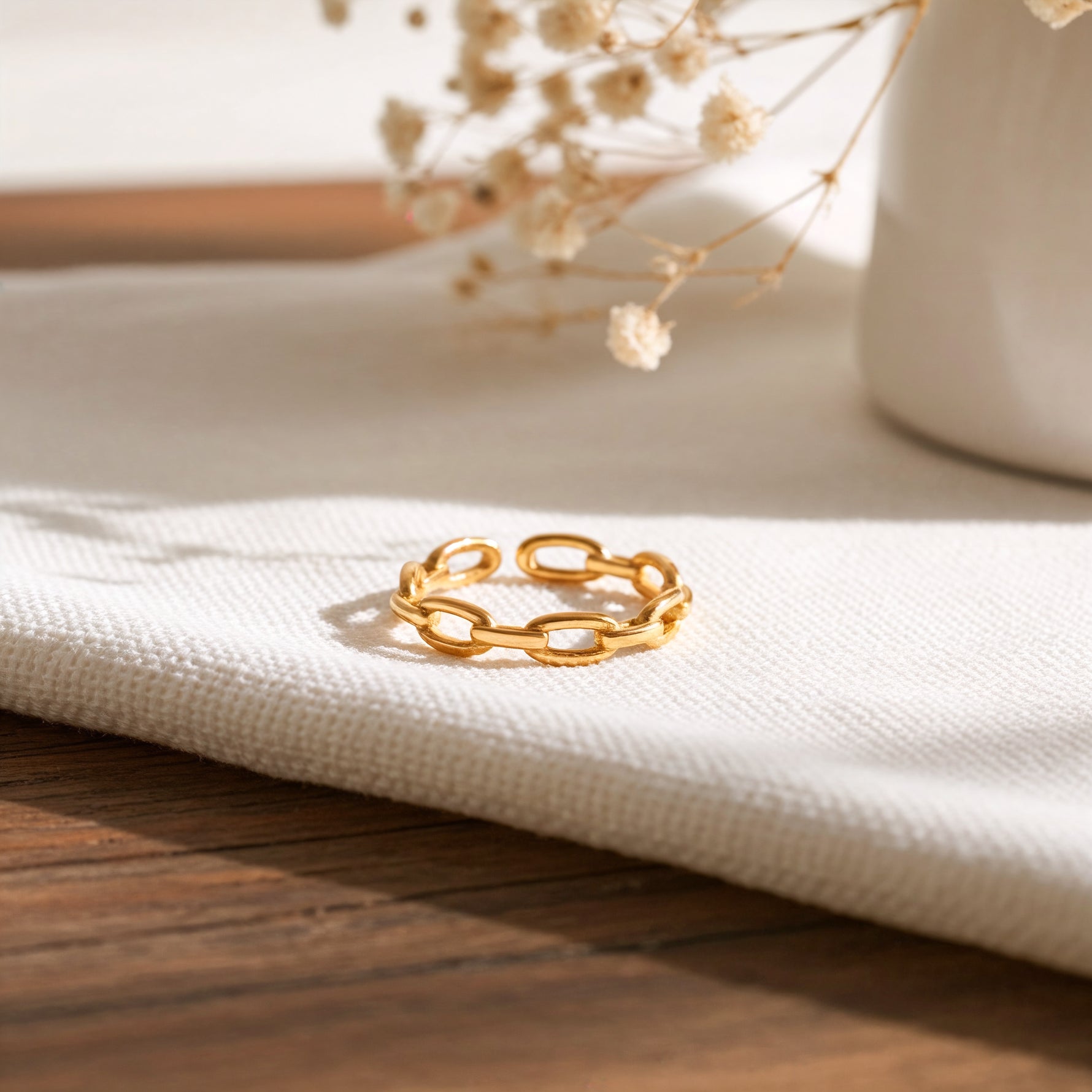 Gliederring aus Edelstahl 18 K vergoldet, offen und verstellbar, mit feiner Kettenstruktur auf hellem Stoffuntergrund und Trockenblumen im Hintergrund – Olyra Ring | Mercy’s Jewelry