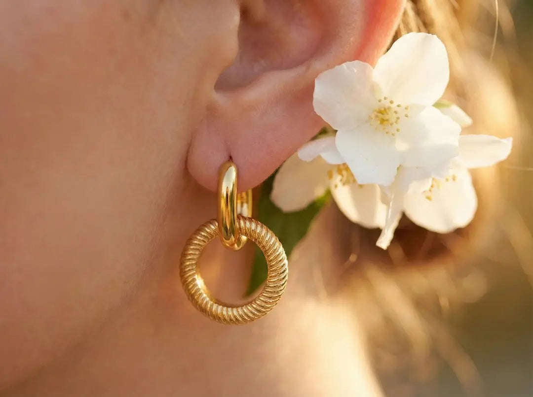 Luxuriöse goldene Creolen Ohrringe der Signature Bloom Kollektion von MERCY'S, in einer eleganten Makroaufnahme am Ohr mit weißer Blüte inszeniert – bymercy.