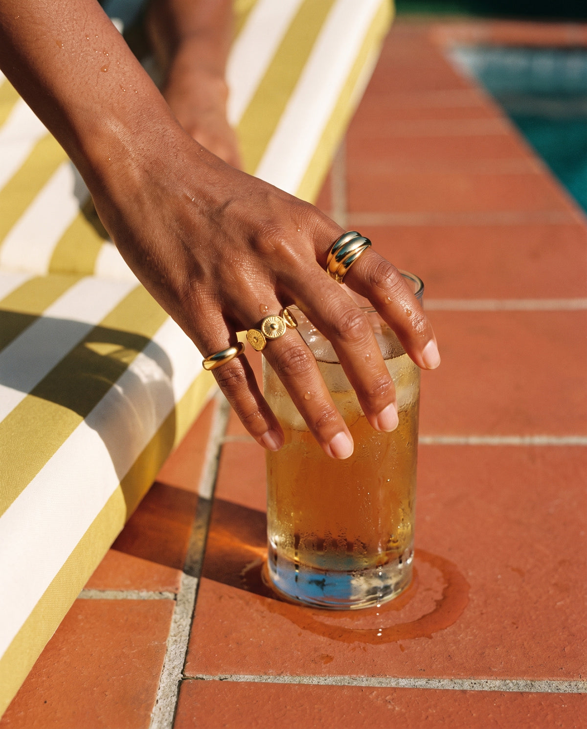 Wasserfeste goldene Ringe von Mercy's an nasser Hand über einem kalten Drink am Pool