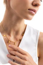 Kaira Halskette – Edelstahl 18K vergoldet, Plättchen-Kette mit goldenen Anhängern, seitlich getragen, Hand am Schlüsselbein