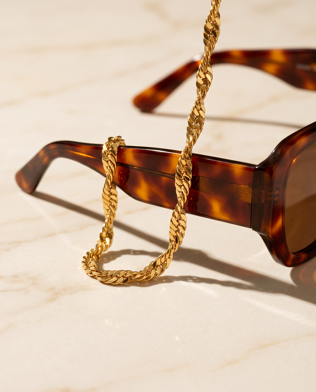 Solira Halskette von Mercy's, feine gedrehte Kette 18K vergoldet, hängt über den Bügel einer Schildpatt-Sonnenbrille auf hellem Marmor im Sonnenlicht