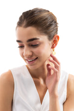 Lachendes Model mit Isara Huggies Ohrringen, goldene Plättchen-Anhänger sichtbar, gefertigt aus Edelstahl, 18K vergoldet