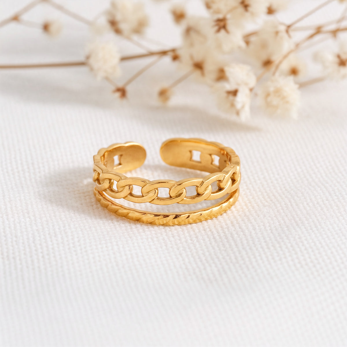 Kettenring aus Edelstahl 18 K vergoldet, offen und verstellbar, mit gehämmerter Struktur und Gliederdesign auf hellem Stoff mit Trockenblumen im Hintergrund – Zelira Ring | Mercy’s Jewelry
