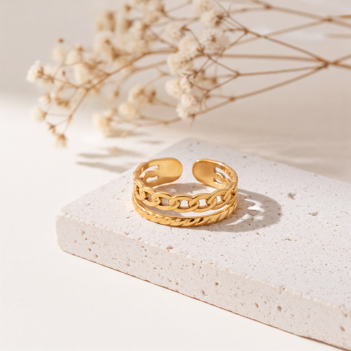 Kettenring aus Edelstahl 18 K vergoldet, offen und verstellbar, mit gehämmerter Struktur und Gliederdesign auf heller Steinplattform mit Trockenblumen im Hintergrund – Zelira Ring | Mercy’s Jewelry