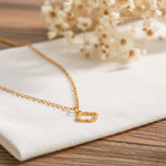 Kleeblatt-Halskette aus Edelstahl 18 K vergoldet, liegt auf hellem Stoff und Holztisch mit Trockenblumen im Hintergrund – Thaleya Halskette | Mercy’s Jewelry