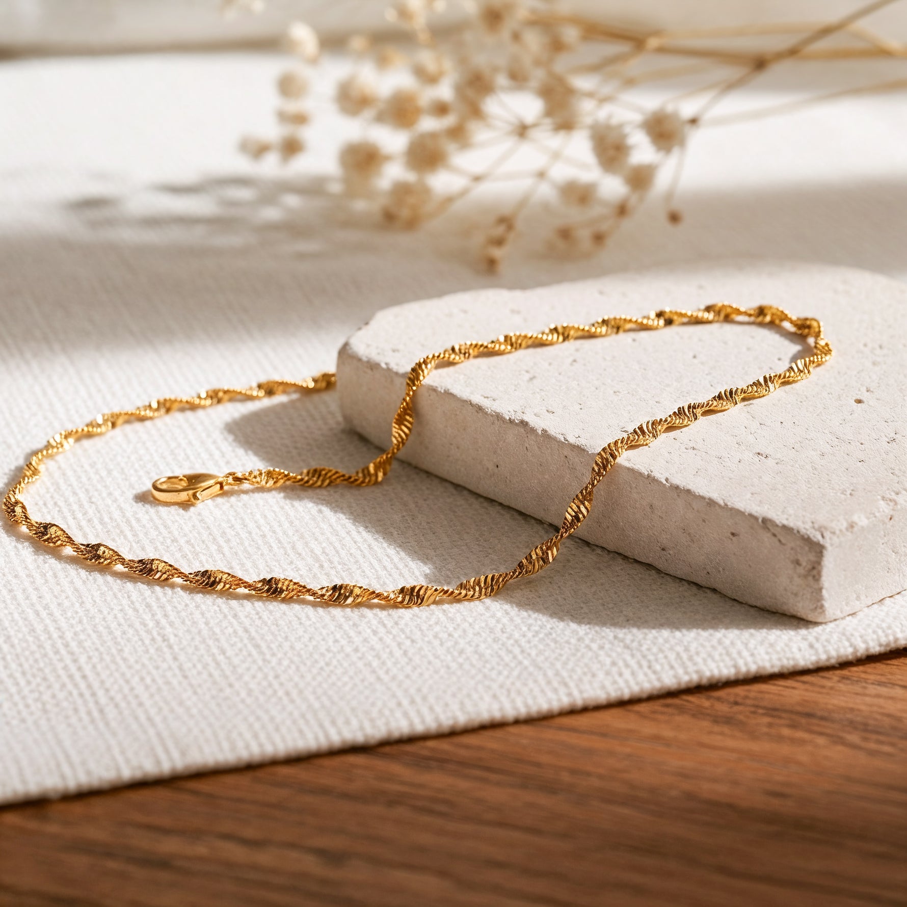 Kordel-Halskette aus Edelstahl 18 K vergoldet, liegt auf hellem Stoff und Holztisch mit Trockenblumen im Hintergrund – Solira Halskette | Mercy’s Jewelry