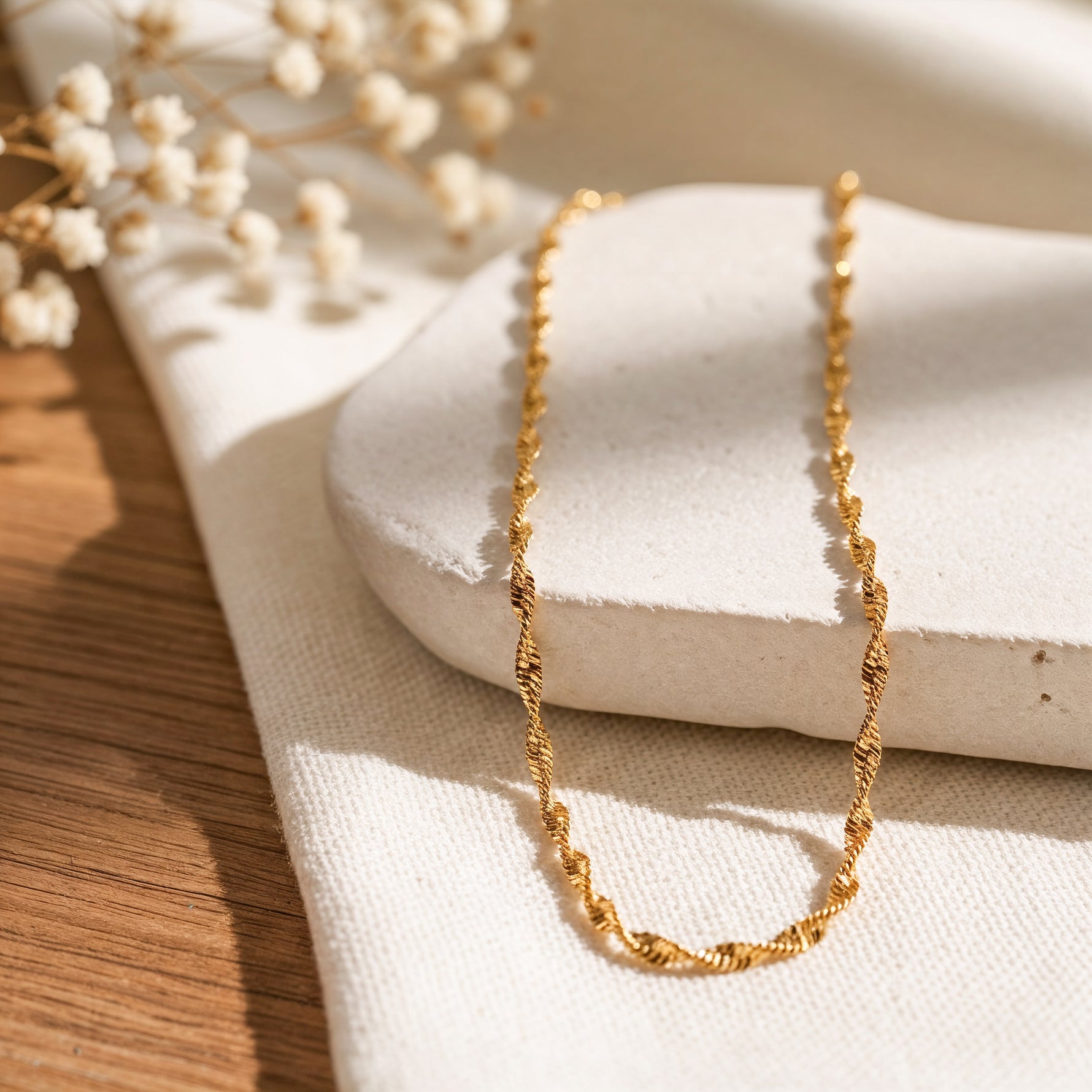 Kordel-Halskette aus Edelstahl 18 K vergoldet, liegt auf hellem Stoff und Steinpodest mit Trockenblumen im Hintergrund – Solira Halskette | Mercy’s Jewelry