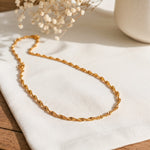 Kordel-Halskette aus Edelstahl 18 K vergoldet, liegt auf hellem Stoff und Holztisch mit Trockenblumen und Vase im Hintergrund – Solira Halskette | Mercy’s Jewelry