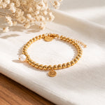 Kugelarmband aus Edelstahl 18 K vergoldet mit Anhänger und Zierperle, elegant auf hellem Stoff mit Trockenblumen – Solina Armband | Mercy’s Jewelry