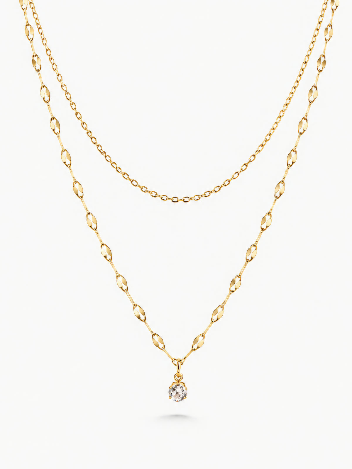 Zweireihige goldene Lirae-Halskette mit feiner oberer Gliederkette und Zirkonia-Anhänger an der längeren Kette vor weißem Hintergrund.