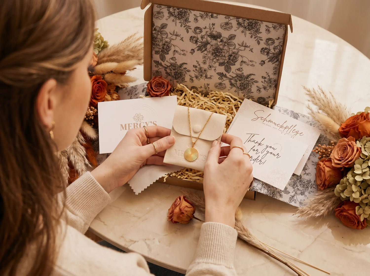 Maria-Anna packt ein MERCY'S Ritual-Paket mit Samtpouch, Manifest-Karte und goldener Halskette von Hand