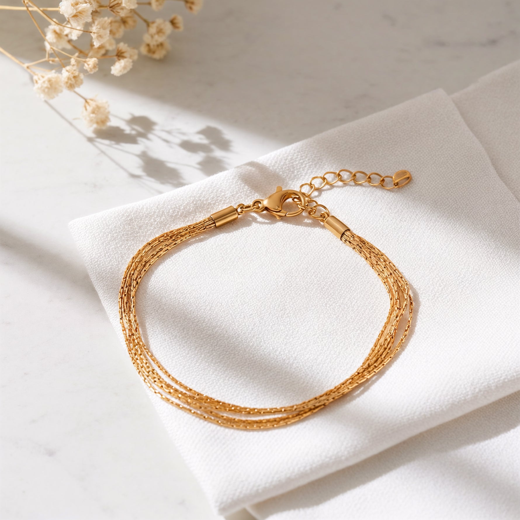 Mehrreihiges Armband aus Edelstahl 18 K vergoldet mit feinen, geflochtenen Strängen, elegant auf weißem Stoff mit sanften Schatten – Vianara Armband | Mercy’s Jewelry