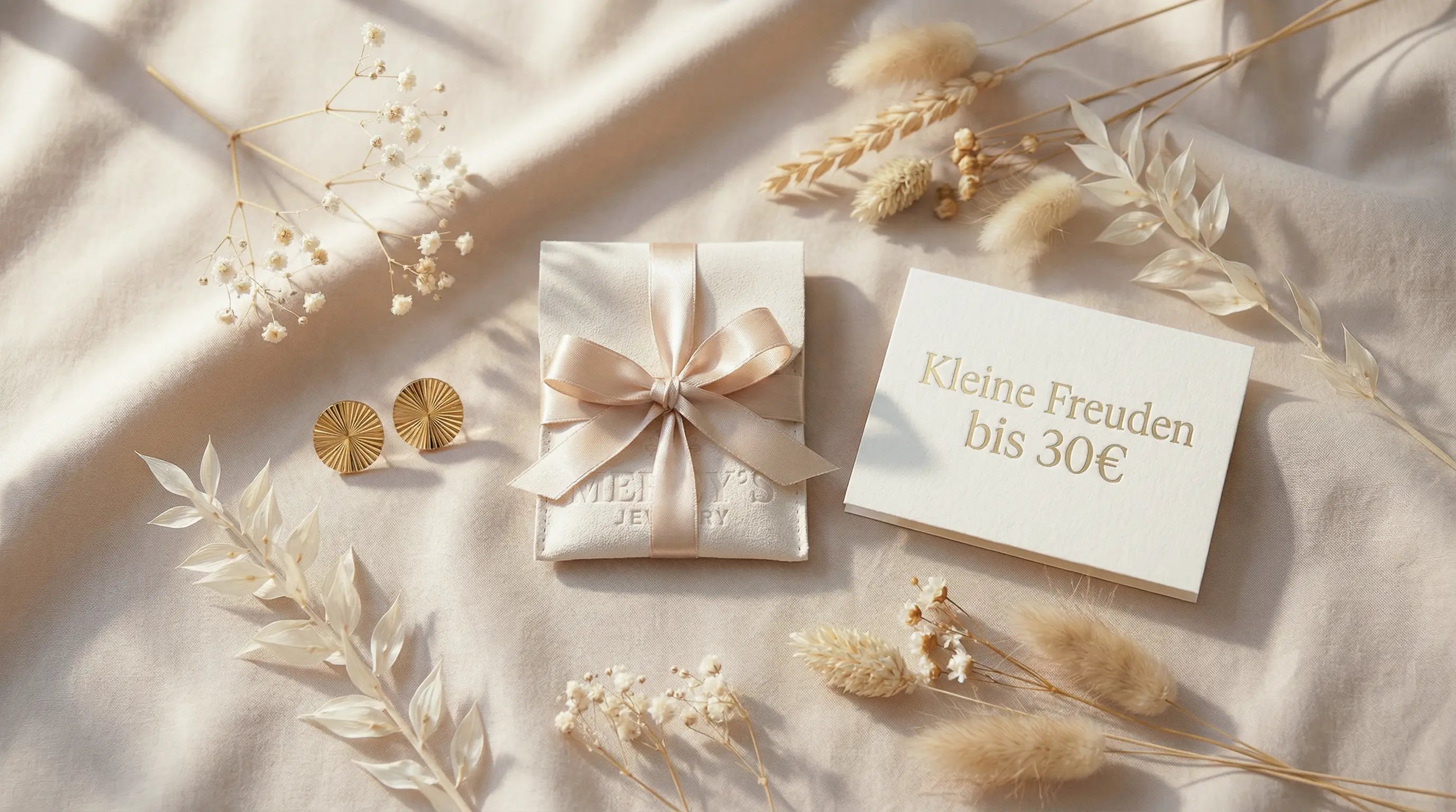 Geschenkidee bis 30 Euro von Mercy’s Jewelry: goldene Ohrringe, beigefarbener Schmuckbeutel mit Schleife und Karte „Kleine Freuden bis 30 €“ in einer hochwertigen Flatlay-Komposition mit Trockenblumen.