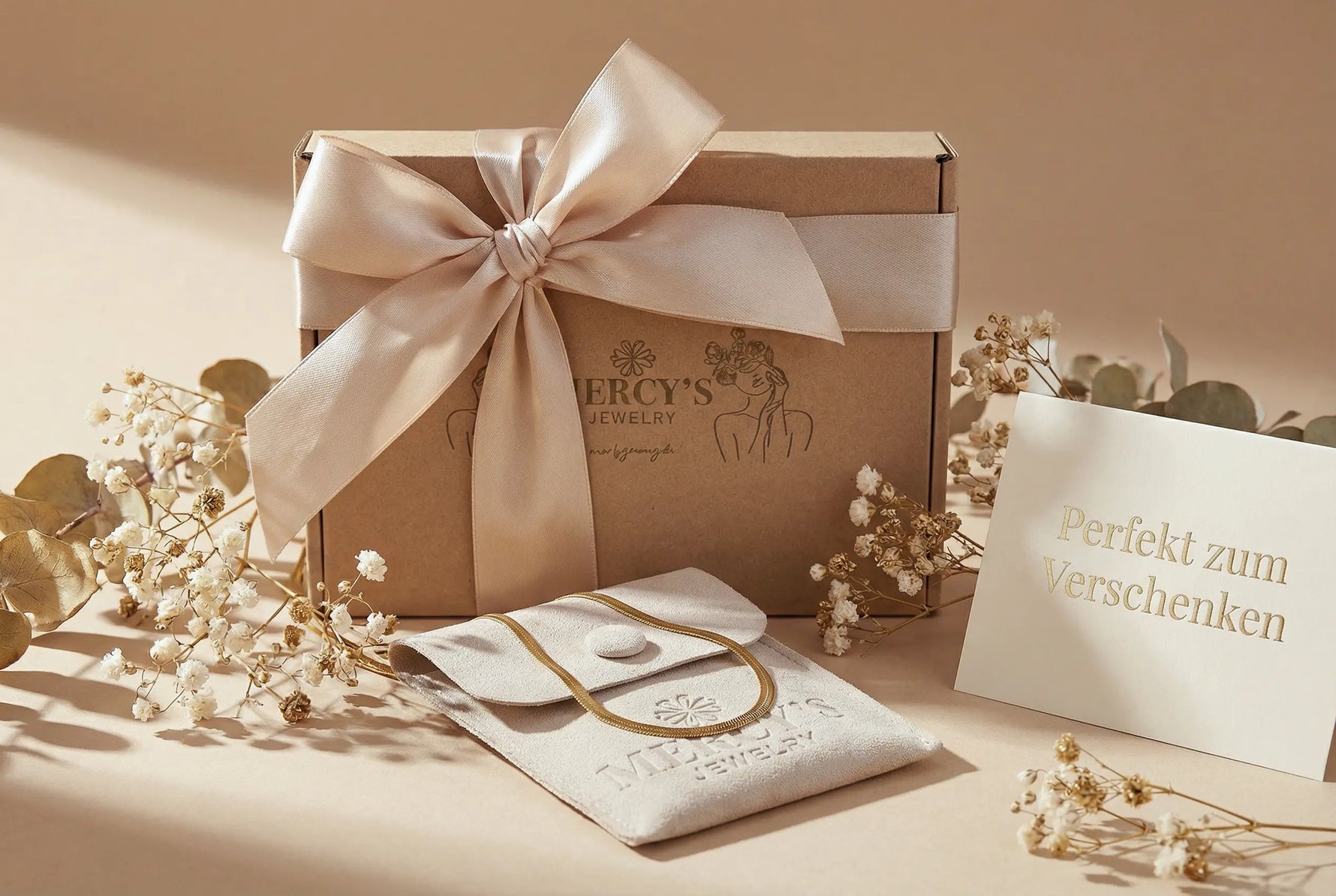 Hochwertige Geschenkbox von Mercy’s Jewelry mit großer Satin-Schleife, Schmuckbeutel und goldener Grußkarte – stilvolle Verpackung zum Verschenken.