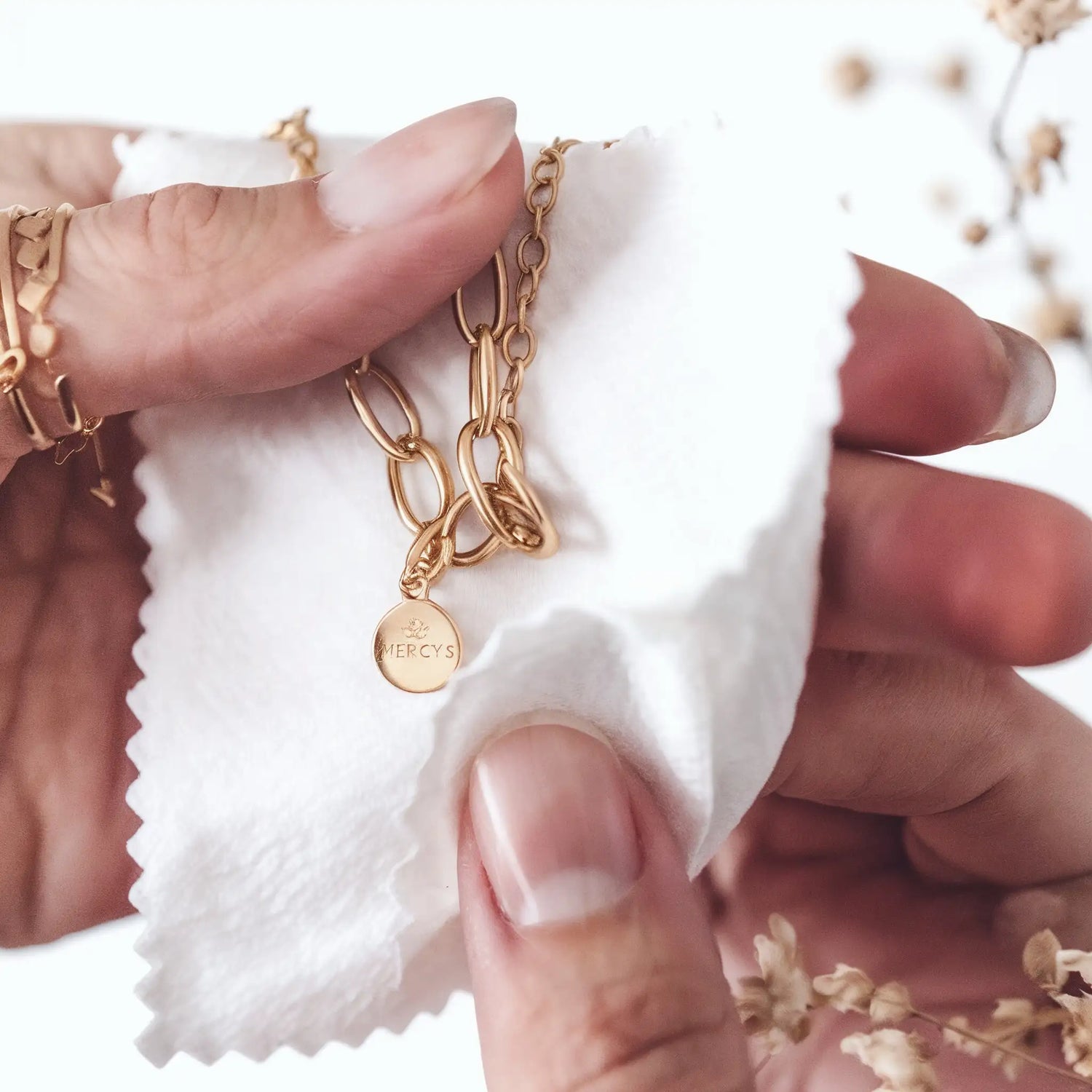 Hände polieren Mercy’s Jewelry goldene Gliederkette mit Gravur-Anhänger mit weißem Schmucktuch