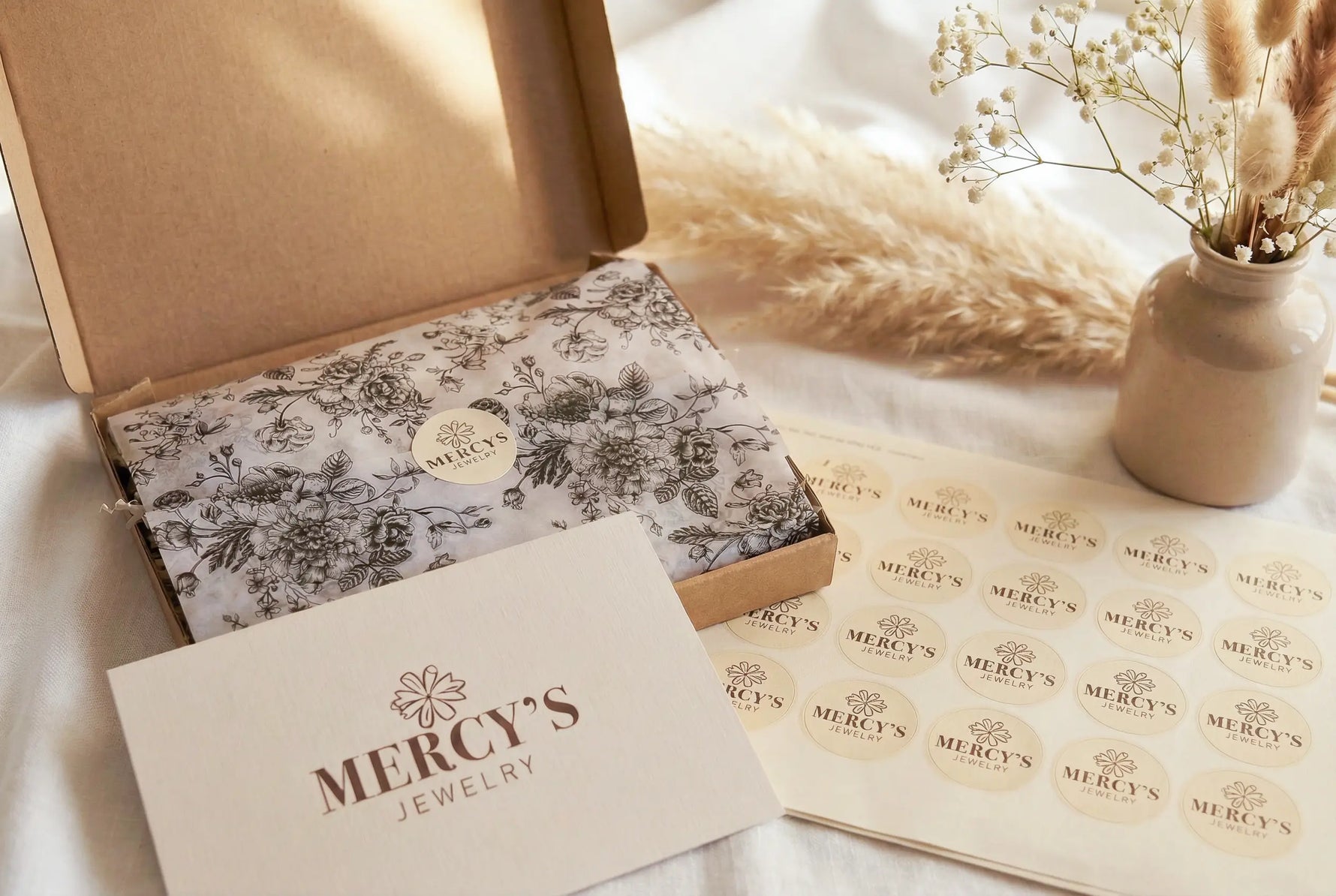 Mercy’s Jewelry Verpackungsset mit Geschenkbox, floralem Seidenpapier, Stickerbogen und Vase mit Pampasgras auf weißem strukturiertem Tuch