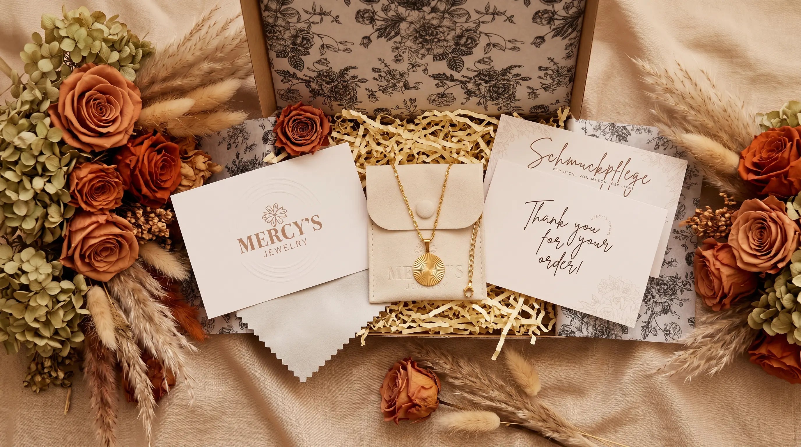 MERCY'S JEWELRY Unboxing Ritual: geöffnete Geschenkbox mit Goldkette, Schmuckbeutel, Pflegekarte und Dankeskarte, umrahmt von getrockneten Rosen und Pampasgras