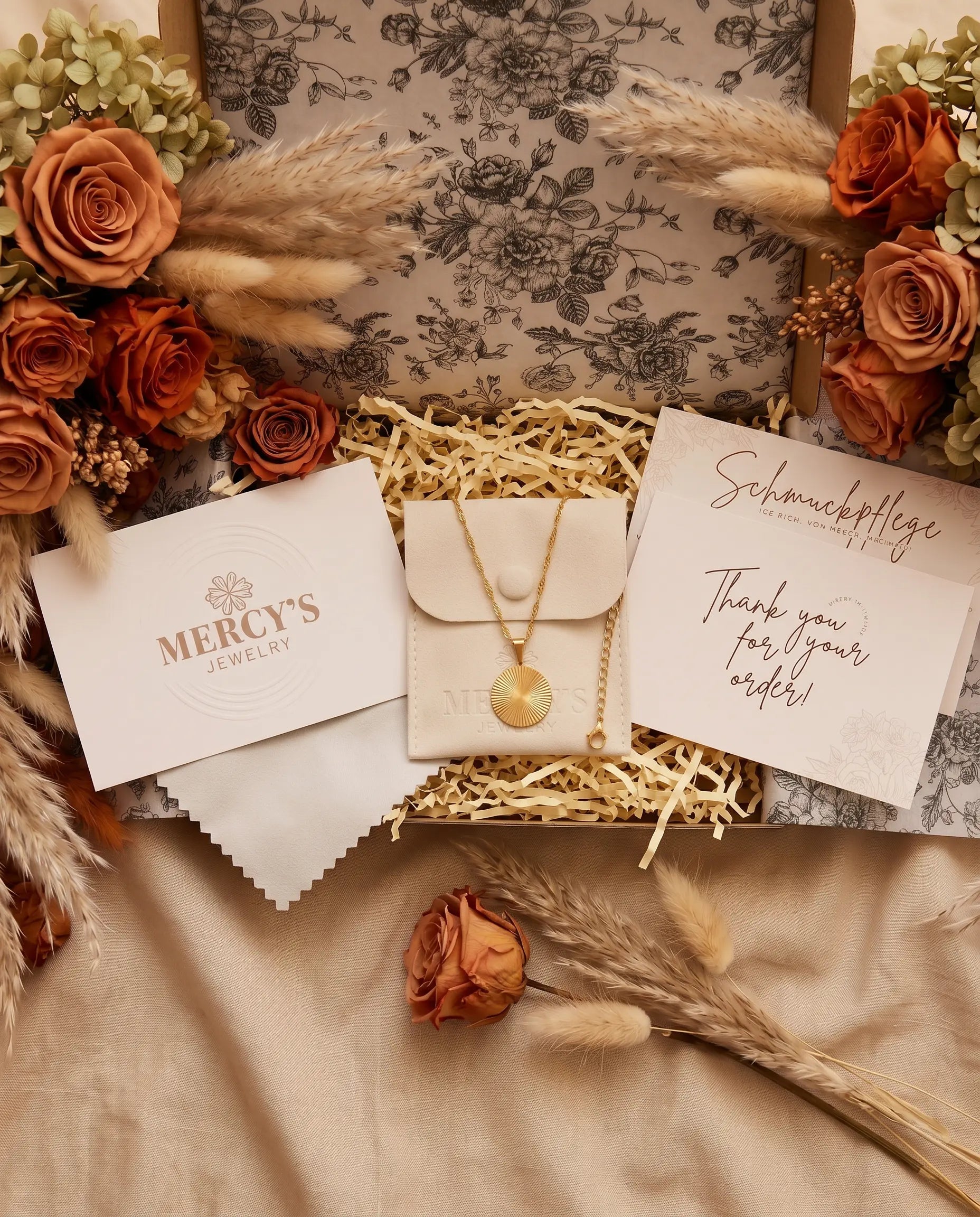 MERCY'S JEWELRY Unboxing Ritual: geöffnete Geschenkbox mit Goldkette, Schmuckbeutel, Pflegekarte und Dankeskarte, umrahmt von getrockneten Rosen und Pampasgras