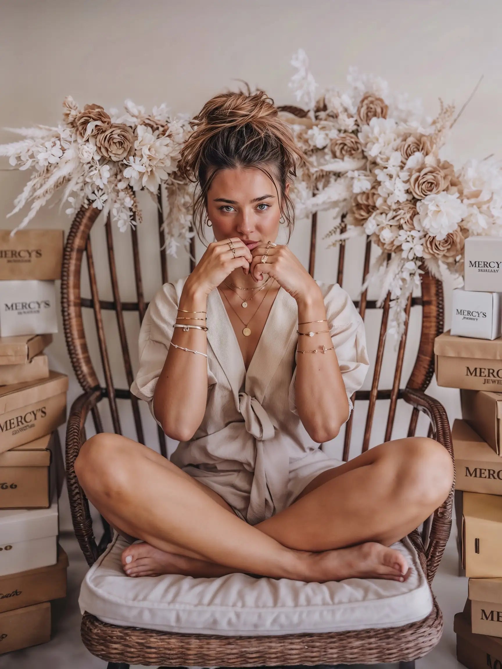 Model trägt Mercy’s Jewelry Schmuck – mehrere goldene Ringe, Halsketten und Armbänder, umgeben von Verpackungsboxen und Blumendeko