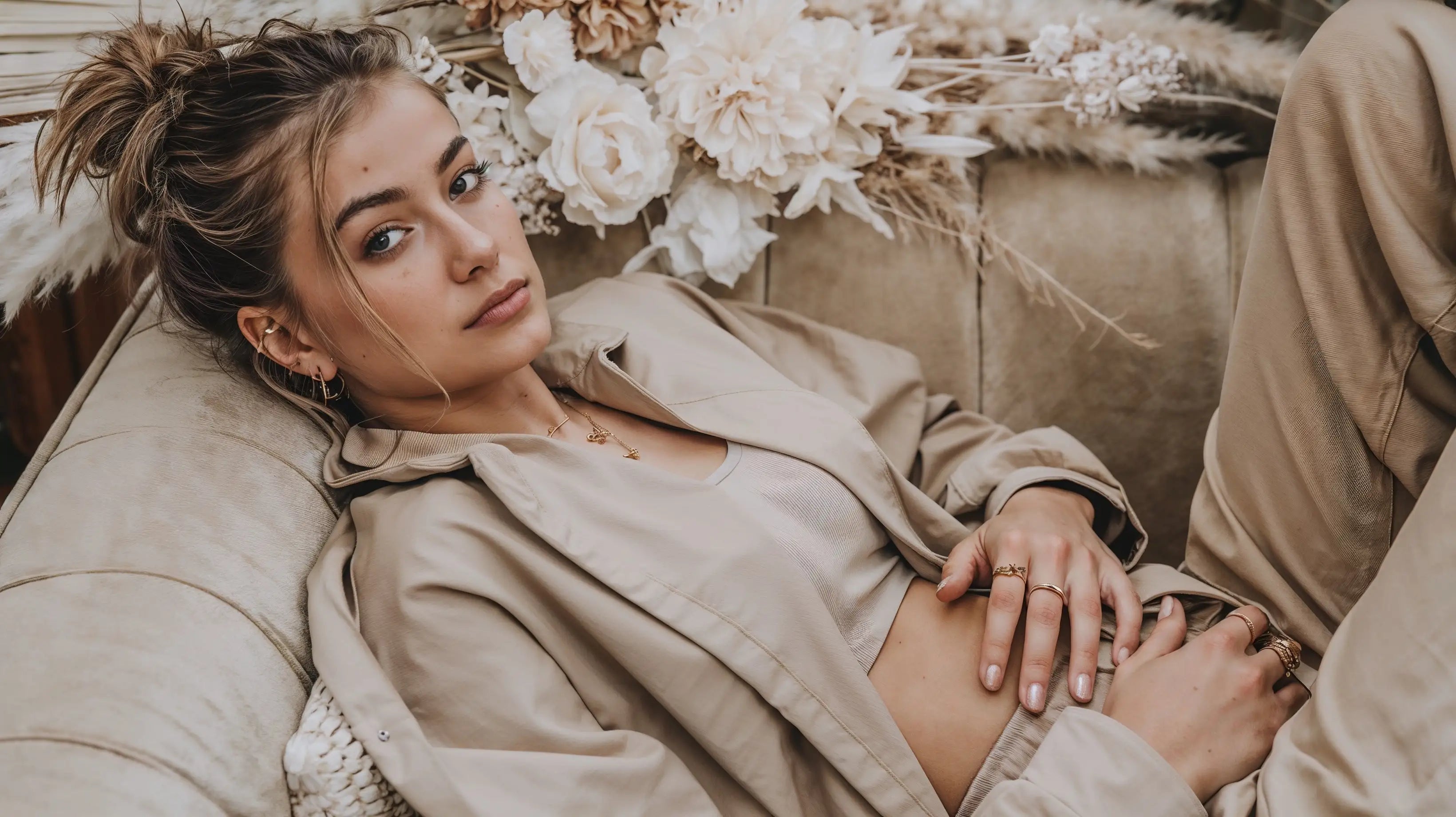 Model liegt entspannt auf Sofa und trägt Mercy’s Jewelry Schmuck – goldene Halskette, Ringe und Creolen