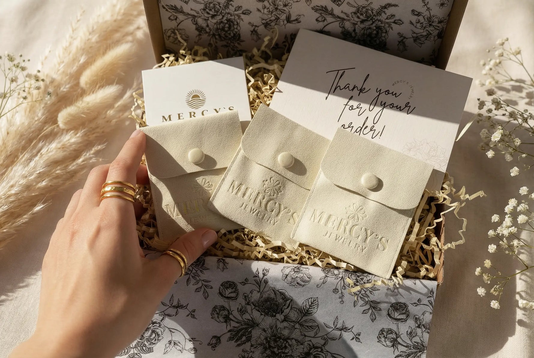 Hochwertiges Mercy’s Jewelry Unboxing mit drei Schmuck-Pouches, Dankeskarte und goldenen Ringen in natürlicher Pampasgras-Deko