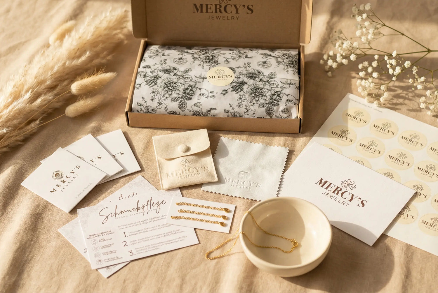 Komplettes Mercy’s Jewelry Verpackungsset mit floralem Seidenpapier, Stickerbogen, Karten, Schmuckpflegehinweis, Samtbeutel, Poliertuch und Schmuckschale – dekoriert mit Pampasgras und Baby’s Breath im warmen Licht.