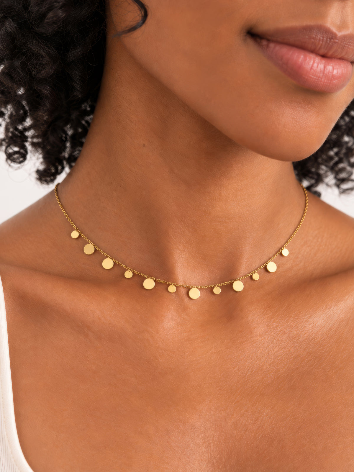 Lyra Plättchenkette in Gold am Hals getragen, mit feinen Kettengliedern und unterschiedlich großen runden Plättchen.