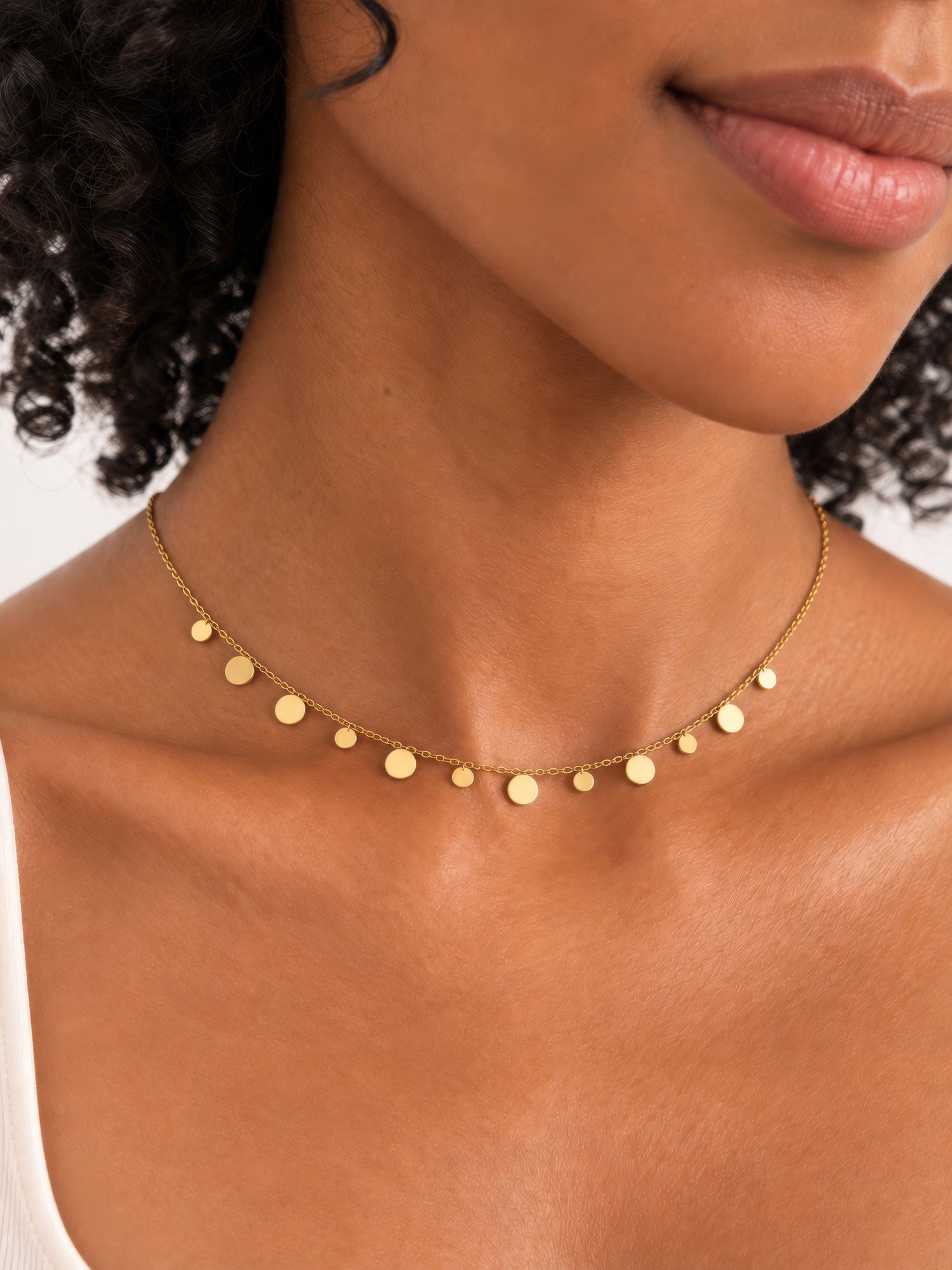 Lyra Plättchenkette in Gold am Hals getragen, mit feinen Kettengliedern und unterschiedlich großen runden Plättchen.