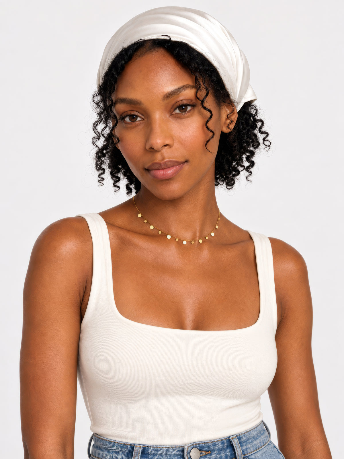 Model trägt die zarte goldene Lyra Plättchenkette zu einem weißen Top und weißem Kopftuch.
