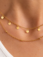 Detailaufnahme der Naia-Halskette auf der Haut mit goldenen Plättchen, feinen Kettengliedern und kleinen Kugeln.